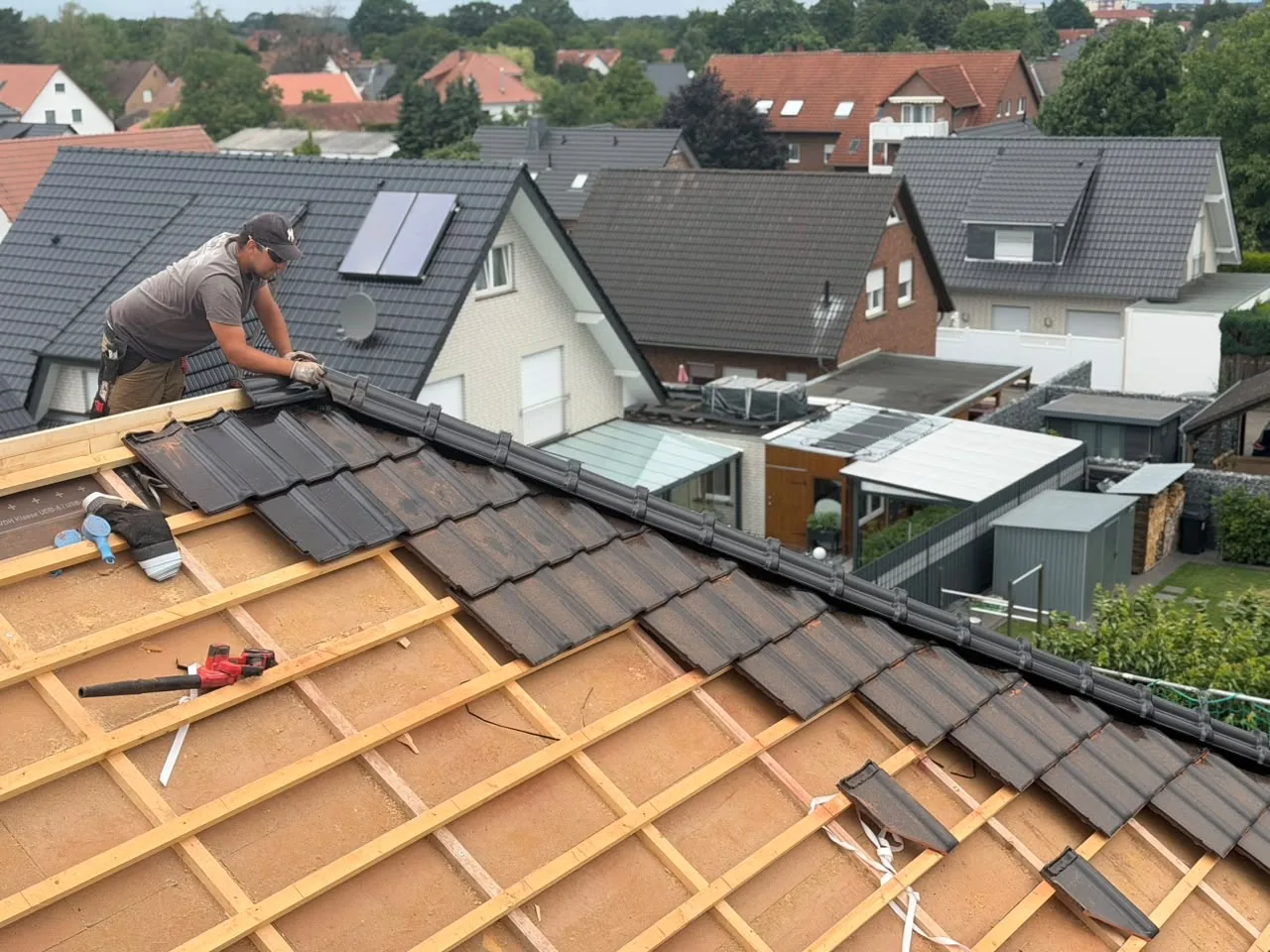 Dachdecker verlegt dunkle Dachziegel auf einer erneuerten Lattung in einem Wohngebiet