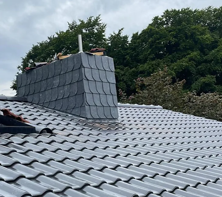 Mit Schieferplatten bekleideter Kamin auf einem dunkel eingedeckten Steildach